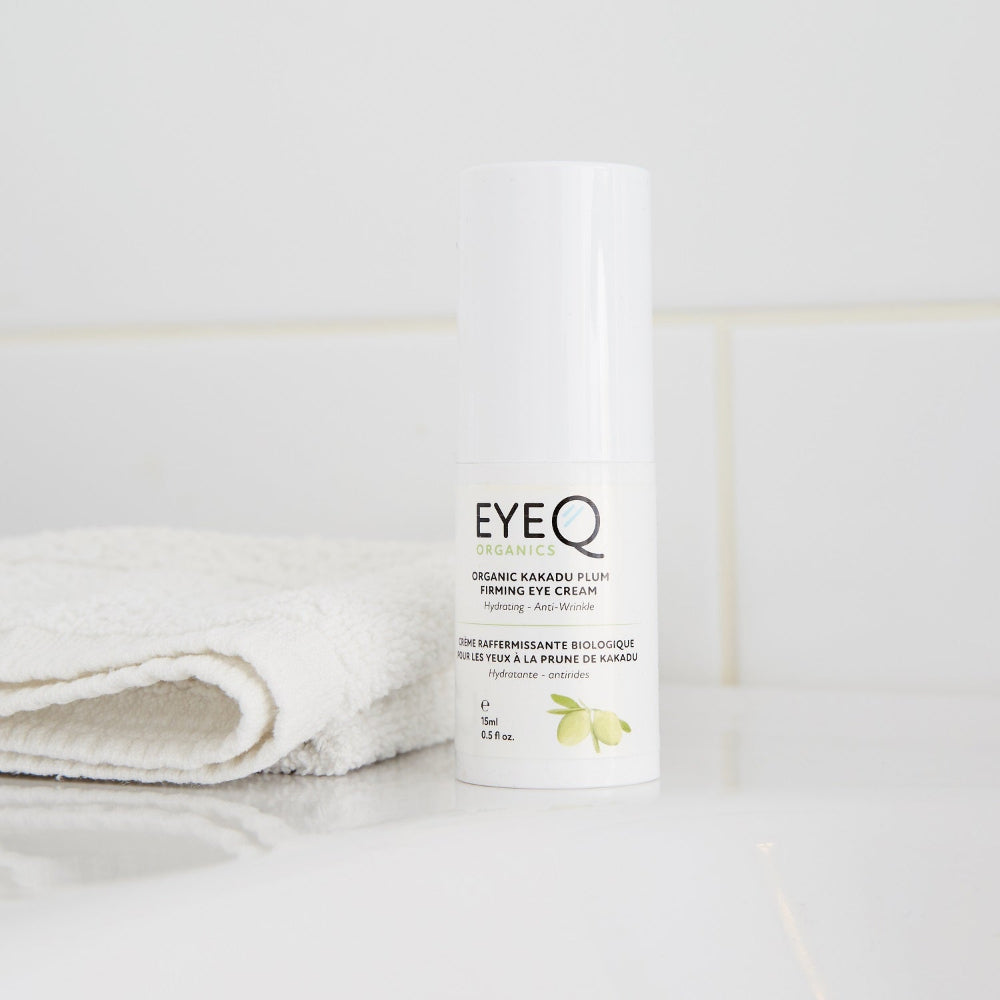 EyeQ eye cream bottle on a white surface with a white towel in the background. The bottle highlights one of the primary sources of vitamin C, Kakadu Plum Seed, paired with Witch Hazel Pulp and Mango Shea Butter to hydrate skin.